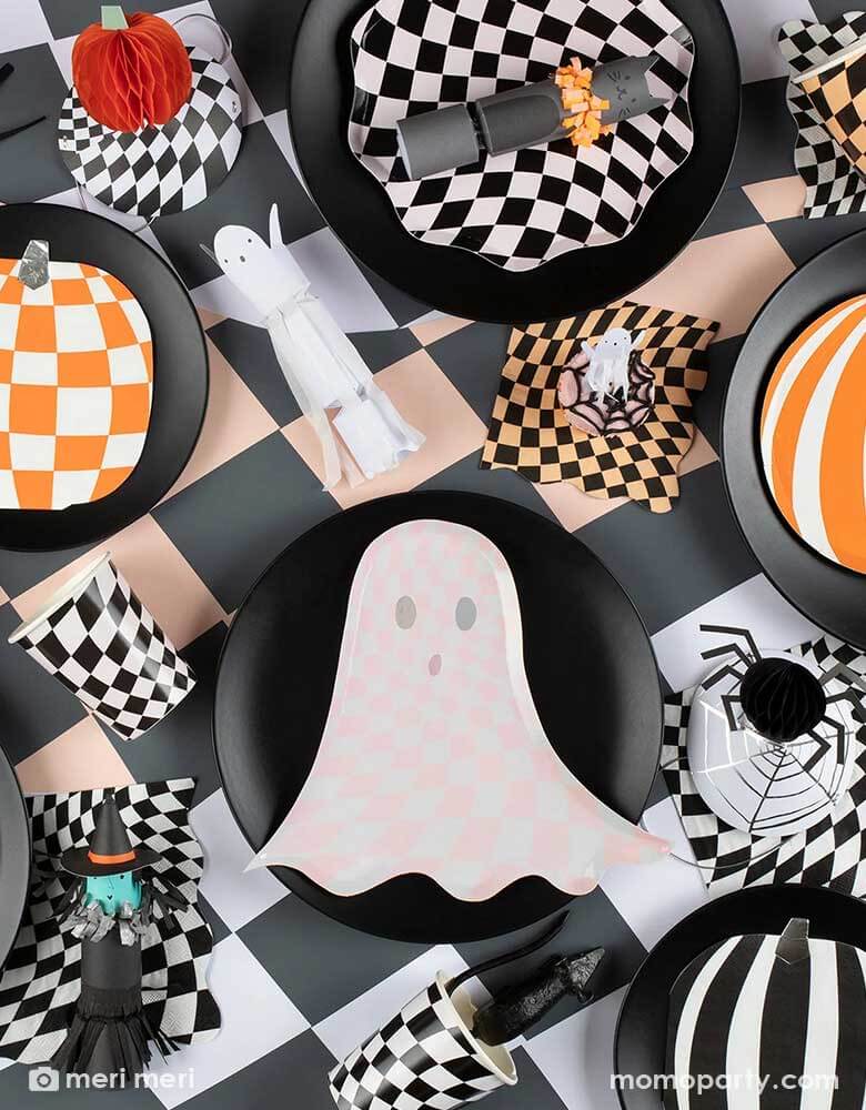 A spooky yet stylish tablescape featuring Momopartys's Halloween wavy checkered plates, napkins and cups by Momopartys, in the middle of the table is the pink ghost shaped plate with chic checkered pattern, it creates a fun inspiration for kid's not-so-spooky Halloween celebration.