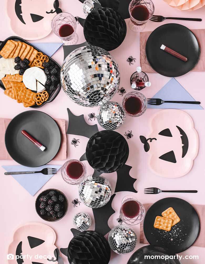 A pink Halloween party table featuring Momopartys's pink Halloween party supplies including pink pumpkin shaped plates, lilac napkins and onyx black round plates as the tableware. In the middle, there are Momopartys's 5.8" bat honeycombs and disco balls as the table centerpiece. There's also some spider confetti spread throughout the pink table, makes it a spooky yet adorable tablescape inspiration for a kid-friendly Halloween party.