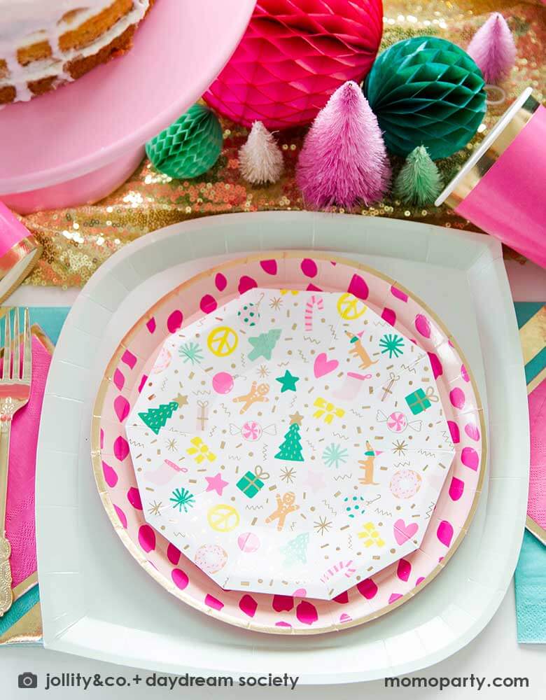 A festive Christmas tablescape featuring Momopartys's Merry and Bright Small Plates by Daydream Society layered with pink dotted round plate and an iridescent dinner plates. Around the plates there are glittered tablecloth, honeycombs and bottle brush Christmas trees in pink shade. Perfect for a chic pink Christmas celebration.