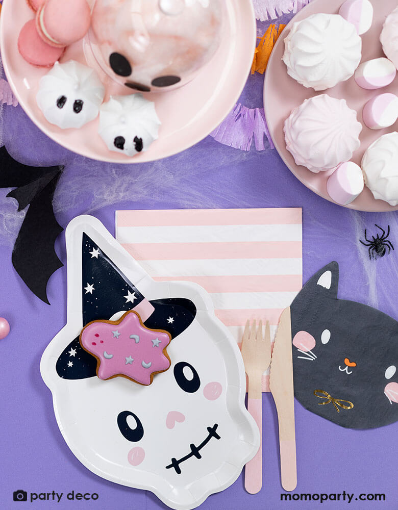 A purple Halloween party table featuring 7" x 10.6" pink skull shaped plate and black cat shaped napkin and pink striped napkin from Momopartys. Around the tableware there are some pink Halloween themed treats including marsh mellows, macaroons, cotton candies, with bat and spider confetti scattered around the table, it makes a great inspiration for a kid-friendly Halloween party.