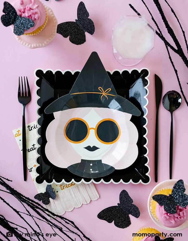 A pink Halloween table featuring Momopartys's 10" x 8" pink witch shaped plate, along with the black scallop edged plates, the pink trick or treat fringe napkins and the glittered butterfly decorations around the tableware, it makes a chic and stylish girly pink Halloween party idea and inspiration.
