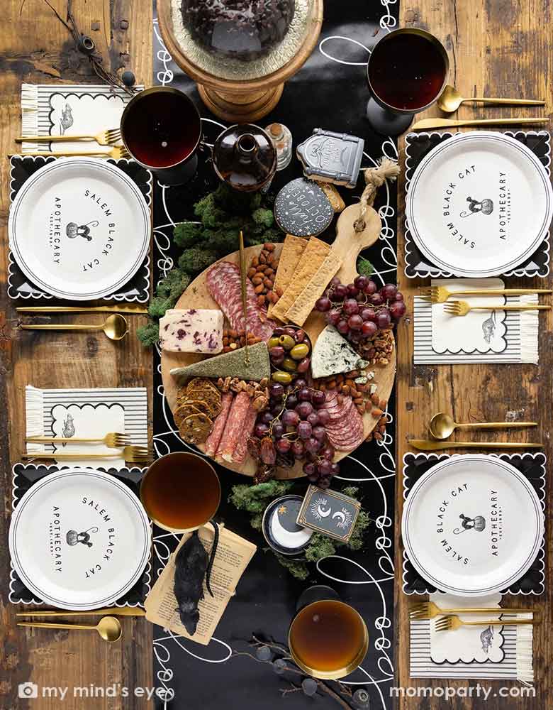 A elegant chic Halloween tablescape featuring Momopartys's Salem-Apothecary-Halloween-party supplies including black and white round plates with black cat design, black scalloped white edged plates and Salem Apothecary Black Ticking Fringe Dinner Napkins by My Mind's Eye. On the table there is Salem Apothecary Boo Table Runner with Halloween themed crescent moon sugar cookies and a charcuterie board board. Makes it a great inspo for an elegant Halloween table.