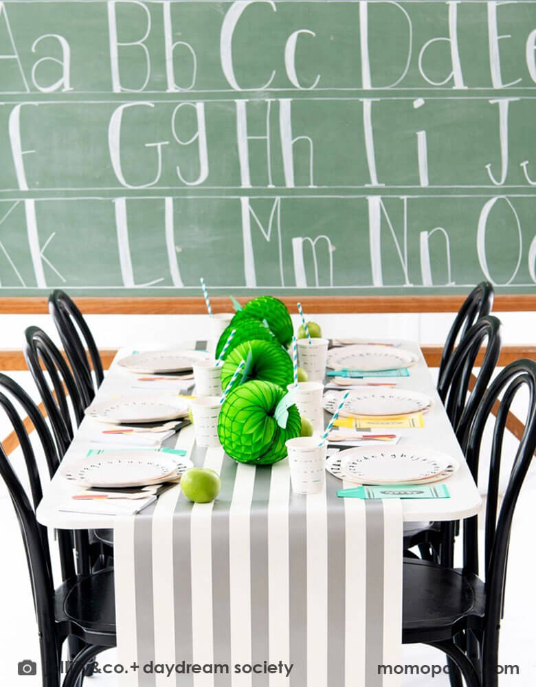 A back to school party table set up in front of a large school chalkboard featuring Momopartys's School Days large and small Plates, along with crayon shaped napkins by Daydream Society. In the middle of the table were some lime green apple honeycombs and green balloons as the centerpiece. All in all makes a great inspiration of a school themed party or first day of school celebration!