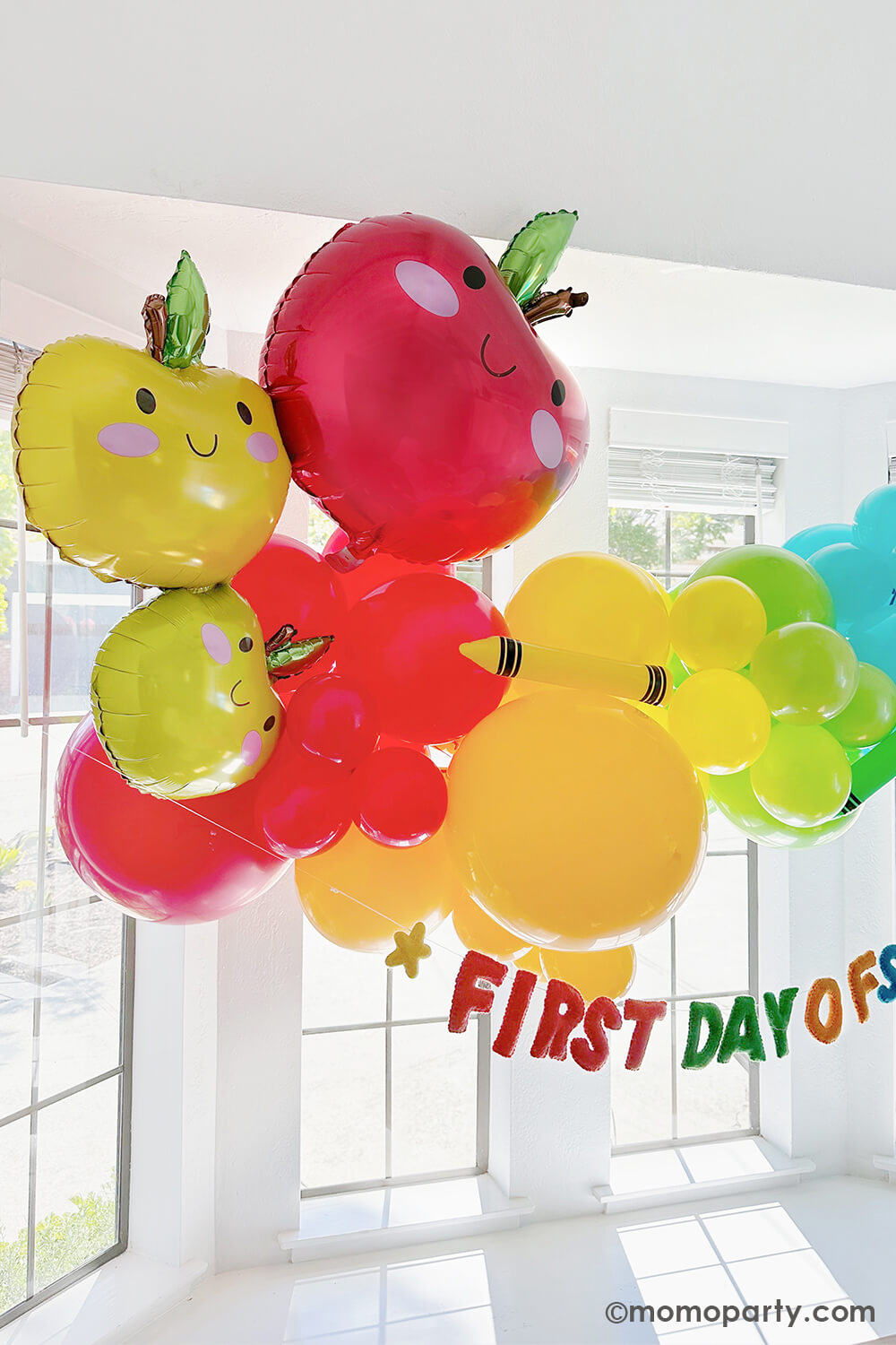 A bright, modern kitchen bay window in the morning decorated with Momopartys's first day of school balloon garlands in fun and bright colors. Underneath is a "first day of school" felt banner by Studio Pep. Along with the adorable apple stacker foil balloon, this makes a great back to school decoration idea and inspiration for any school themed celebration!