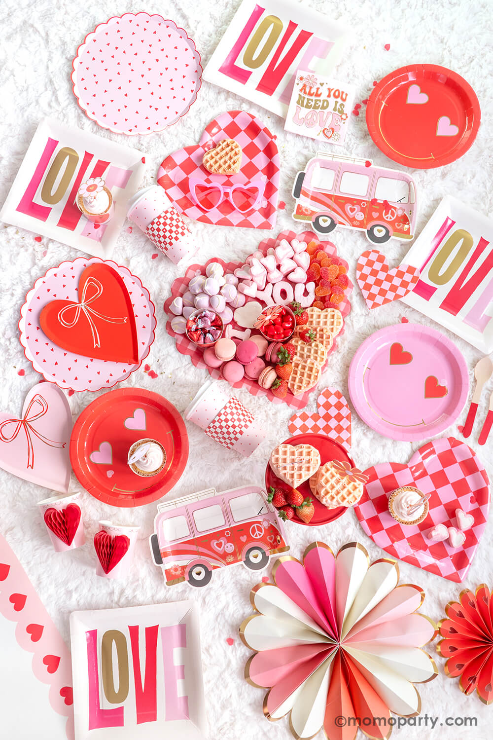 Top view displayed Momopartys's 2024 Valentine's Day party collection. Featuring  Heart Pattern Dinner Plates, Heart With Bow Plates, Honeycomb Heart Cups, Occasions by Shakira - Luv Bus Paper Plates, and All You Need is Love Napkins. Also, Checkered Heart-Shaped Paper Plates, Square Love Paper Plates, Heart Eyes Paper Plates, Red Checks To-Go Cup Set, and Pink Heart Border Paper Table Runner. Not to forget the Checkered Heart-Shaped Tray adorned with sweet treats, for a festive Valentine's celebration