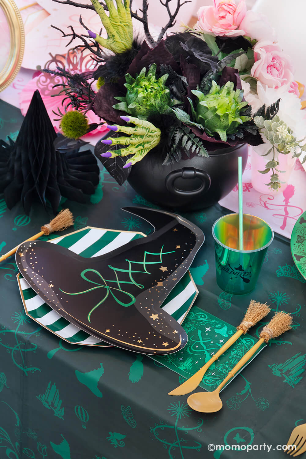 A Wicked themed party table setting with various of Momopartys's Wicked themed party supplies including the wicked witch hat shaped plate, emerald green striped dinner plate, the Wicked green napkin inspired by Elphaba, witchbroom shaped utensil set, and wicked green party cup with green iridescent straw on the green and pink two-tone Wicked tablecloth. With Wicked inspired floral bouquet and witch hat honeycomb centerpiece, it makes a whimsical and mystical Halloween celebration in this spooky season!
