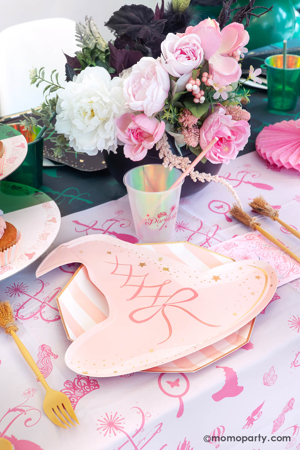 One side of Wicked themed party table setting inspired by Glinda with various of Momopartys's Wicked themed party supplies including the pink witch hat shaped plate, pink striped dinner plate, the  Wicked pink napkin inspired by Glinda, witch broom shaped utensil set, and Glinda pink party cup with pink iridescent straw on the pink and green two-tone Wicked tablecloth. With Glinda inspired floral bouquet, it makes a great setting for an enchanting Wicked themed celebration.