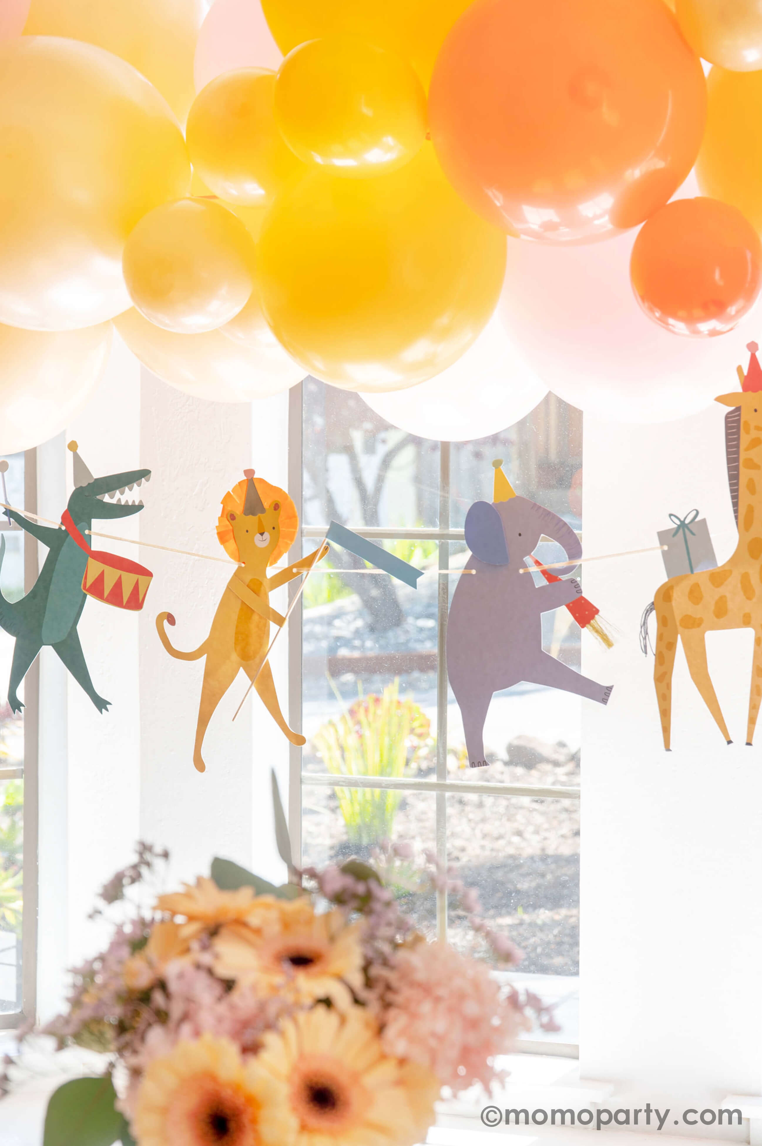 A kid's animal themed party decoration idea featuring Momopartys's adorable animal parade birthday garland featuring a lion, an elephant, an alligator, a giraffe, along with a festive balloon garland in a warm color tone in the back, it makes a great party inspiration for kid's animal, safari, carnival themed birthday party.