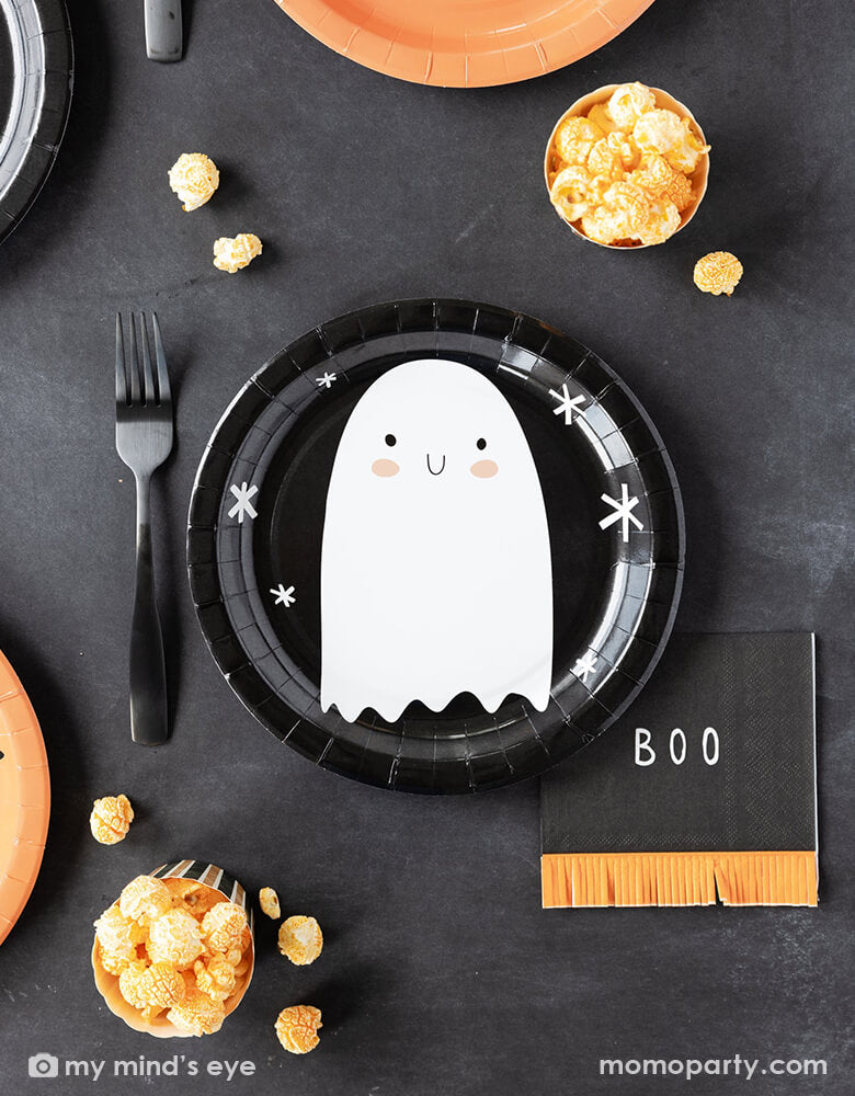 A kid's friendly Halloween party tablescape features Momopartys's classic Halloween party supplies including the friendly ghost black round plate, the boo fringe small napkins, and the orange and black striped food cups filled with popcorn. This simple and modern place setting provide an effortless yet festive idea for celebrating Halloween with kids this spooky season.