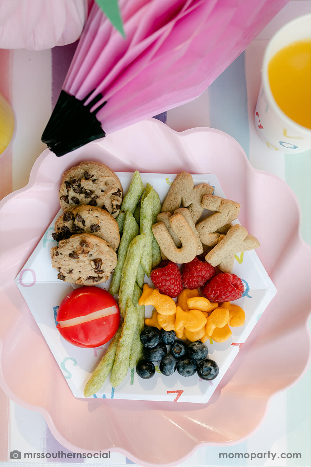 A pastel back to school party table food snack ideas by Mary at Mrs Southern Social. Featuring Momopartys's back to school party supplies including ABC alphabet plates, napkins, and party cups. One the plates are kids snack ideas including fruits, cheeses, goldfish, ABC alphabet crackers. With pastel rainbow striped placemats and pastel rainbow pencil honeycombs and pink apple honeycombs, all together makes an adorable tablescape for kid's first day of school celebration.