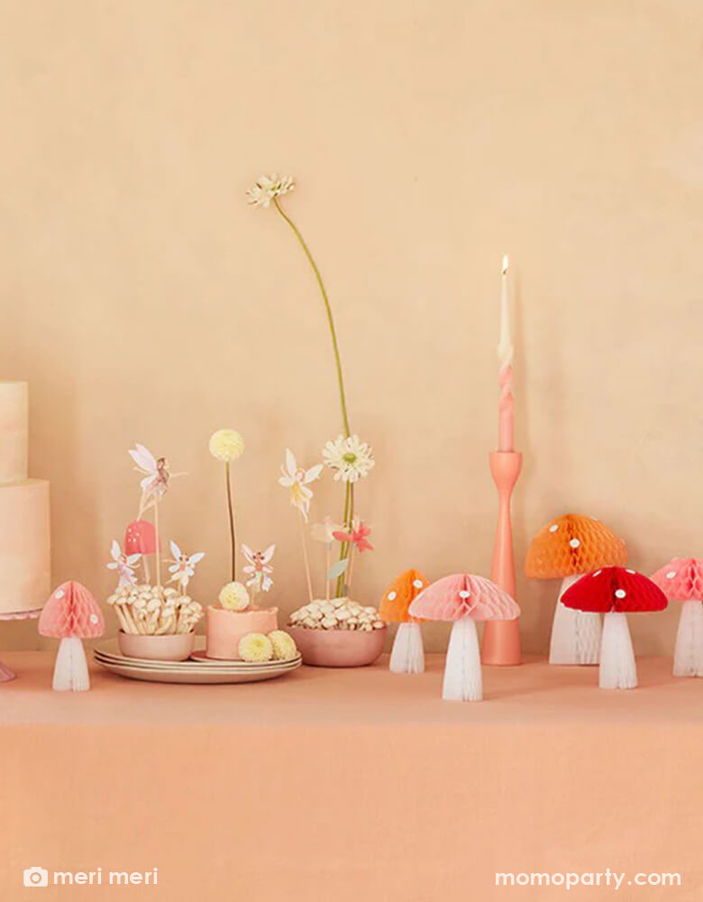 A whimsical fairy themed birthday party table featuring Momopartys's mushroom honeycombs and fairy cake toppers. A few small cupcakes are topped with fairy cupcake toppers and cake topper and adorn with buttercream flowers, makes this a simple yet whimsy party inspo for kid's forest fairy themed party.