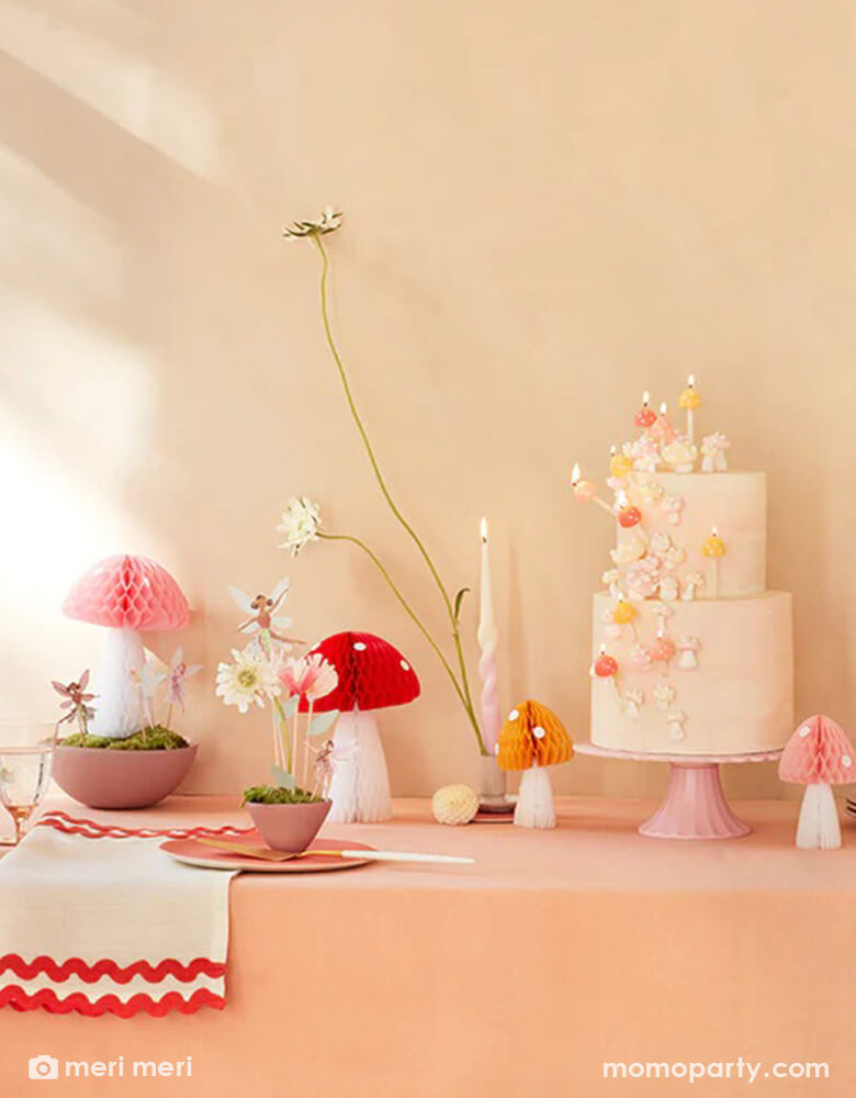 A whimsical fairy themed birthday party table featuring Momopartys's mushroom honeycombs and fairy cake toppers. A 2-tier cake is topped with mushroom candles and adorn with buttercream flowers, makes this a simple yet whimsical party inspo for kid's forest fairy themed party.