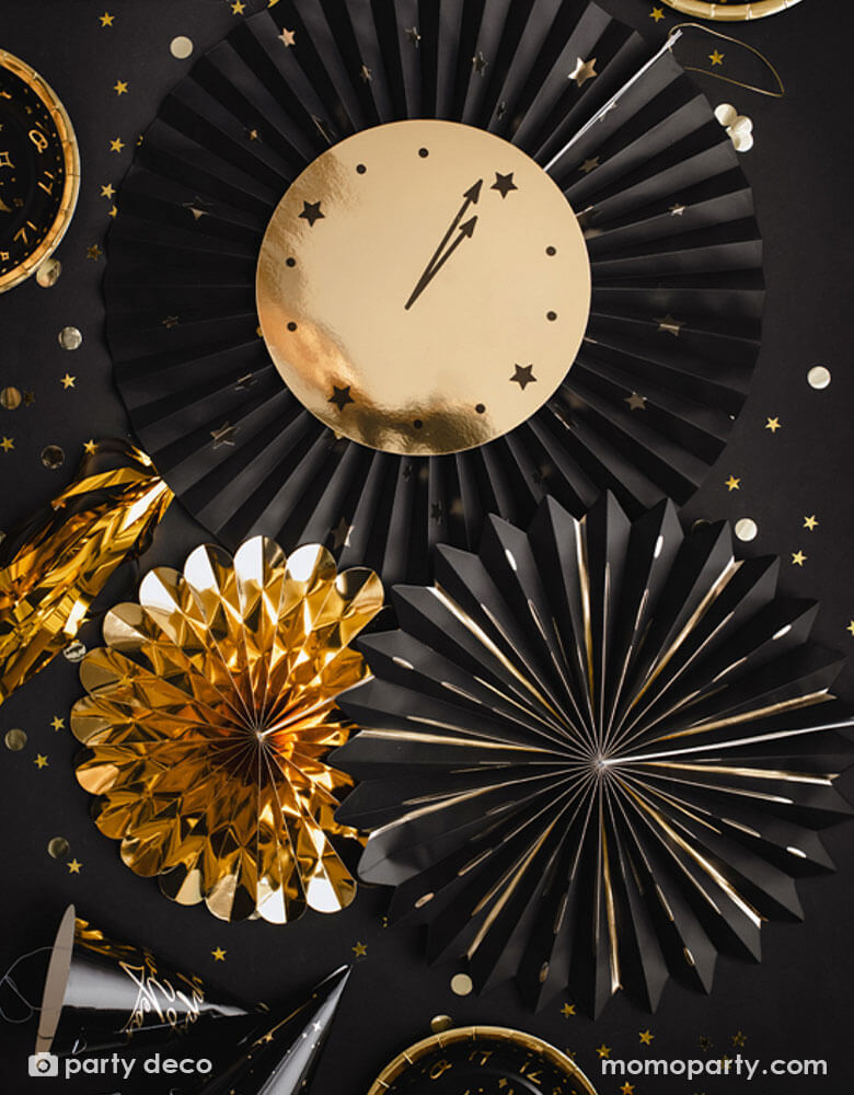 A black party table filled with confetti and new year party hats around Momopartys's New Year Countdown Party Fans by Party Deco. Comes with 3 party fans in the size of 26 cm, 35 cm, 43 cm in gold and black, this paper fan set with a paper clock on it is perfect for your New Year's Eve Countdown party.