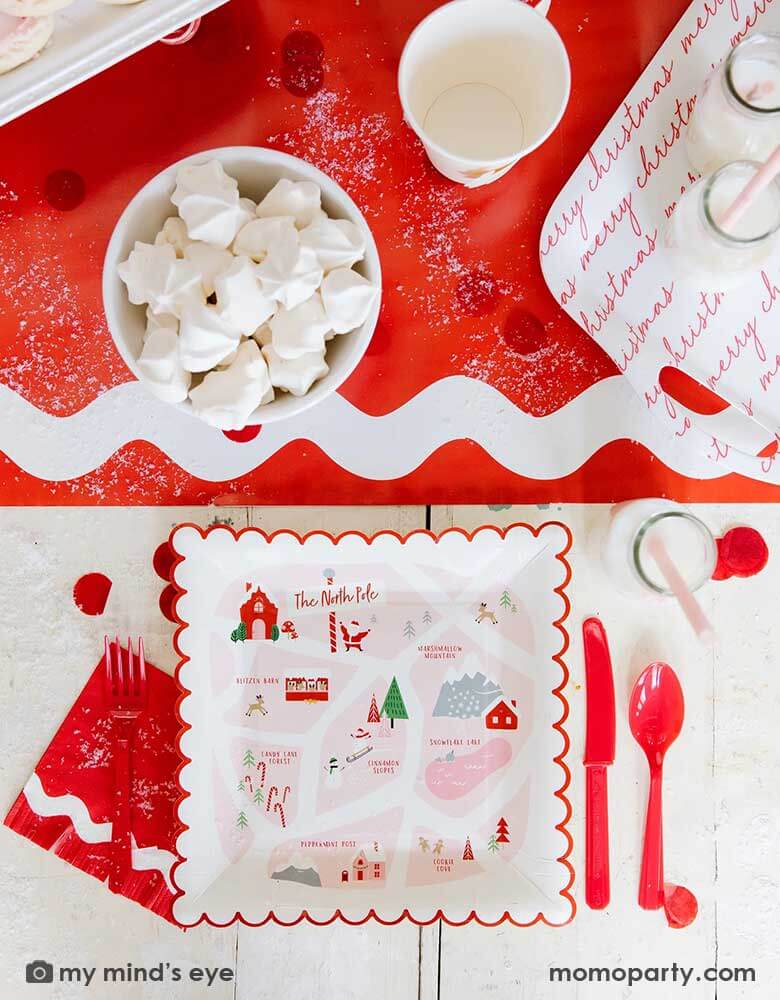 A festive Santa & Elf inspired red tablescape featuring Momopartys's Believe North Pole Map red scallop-edged 9" x 9" plates by My Mind's Eye, Elf inspired ric rac small fringe napkins, some milk bottles, and Santa face shaped party cups next to a red and white bamboo tray on ric rac red table runners, all makes a great inspo for a festive Holiday table setting.