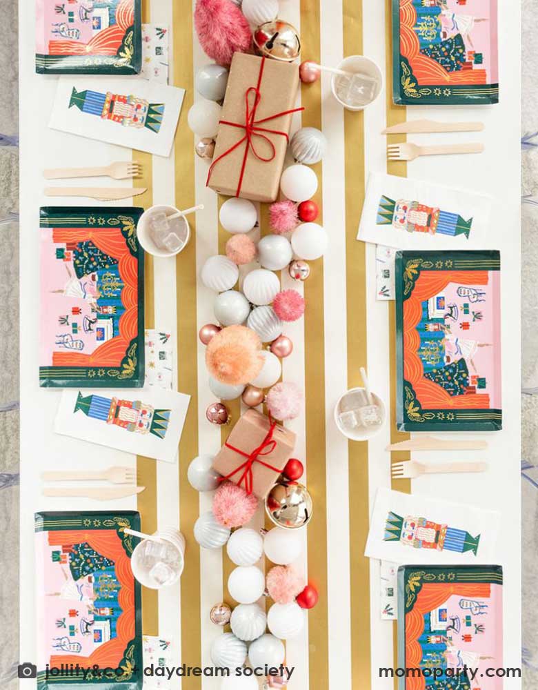 A festive Nutcracker themed holiday party table featuring Nutcracker themed party tableware from Momopartys including 11" x 6.5" Nutcracker magical large plates, Nutcracker guest napkins, red striped party cups and gold striped table runner. In the middle of the table there are Christmas tree ornaments, gifts, mini Christmas trees and Nutcracker decorations.