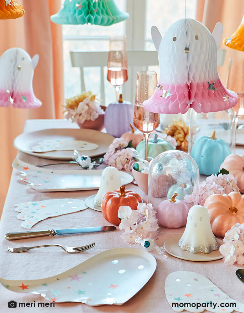 A festive pastel themed Halloween party table decoration featuring Momopartys's ghost with pastel stars plates and napkins by Meri Meri. On the table three are pastel colored pumpkins, autumn flower arrangement and ghost shaped candles are the centerpiece, along with Meri Meri's honeycomb ghost hanging decorations dipped with pastel colors and silver foil stars, this soft and sweet set up makes a great inspo for a kid's non-scary halloween party decorating ideas!