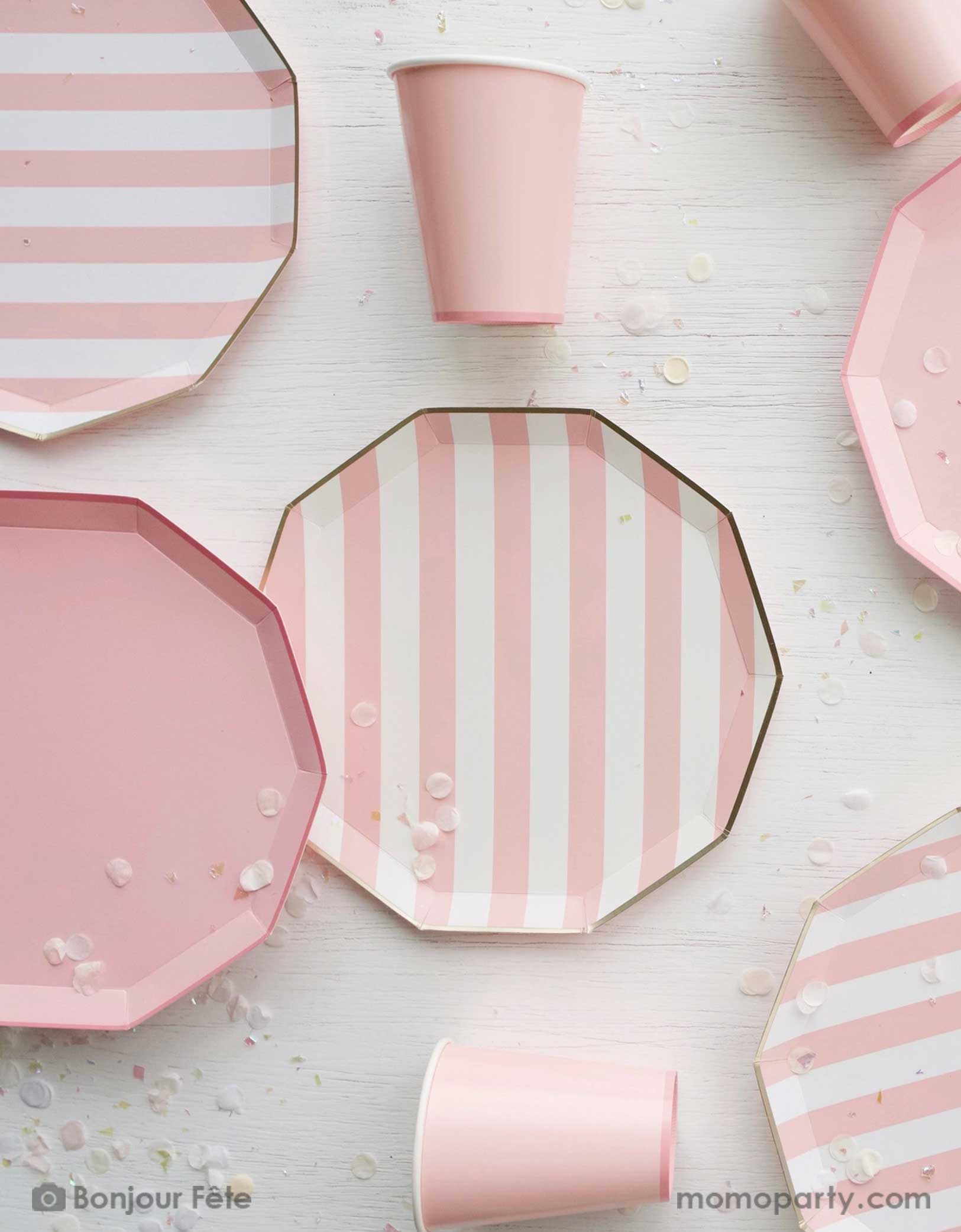 An overhead shot of a party table filled with Momopartys's pastel pink themed party tableware including pastel pink cabana striped dinner plates and pastel pink dinner plates in decagon shape with matching party cups, with pale pink confetti - a great collection for girl's birthday or a baby girl shower. 