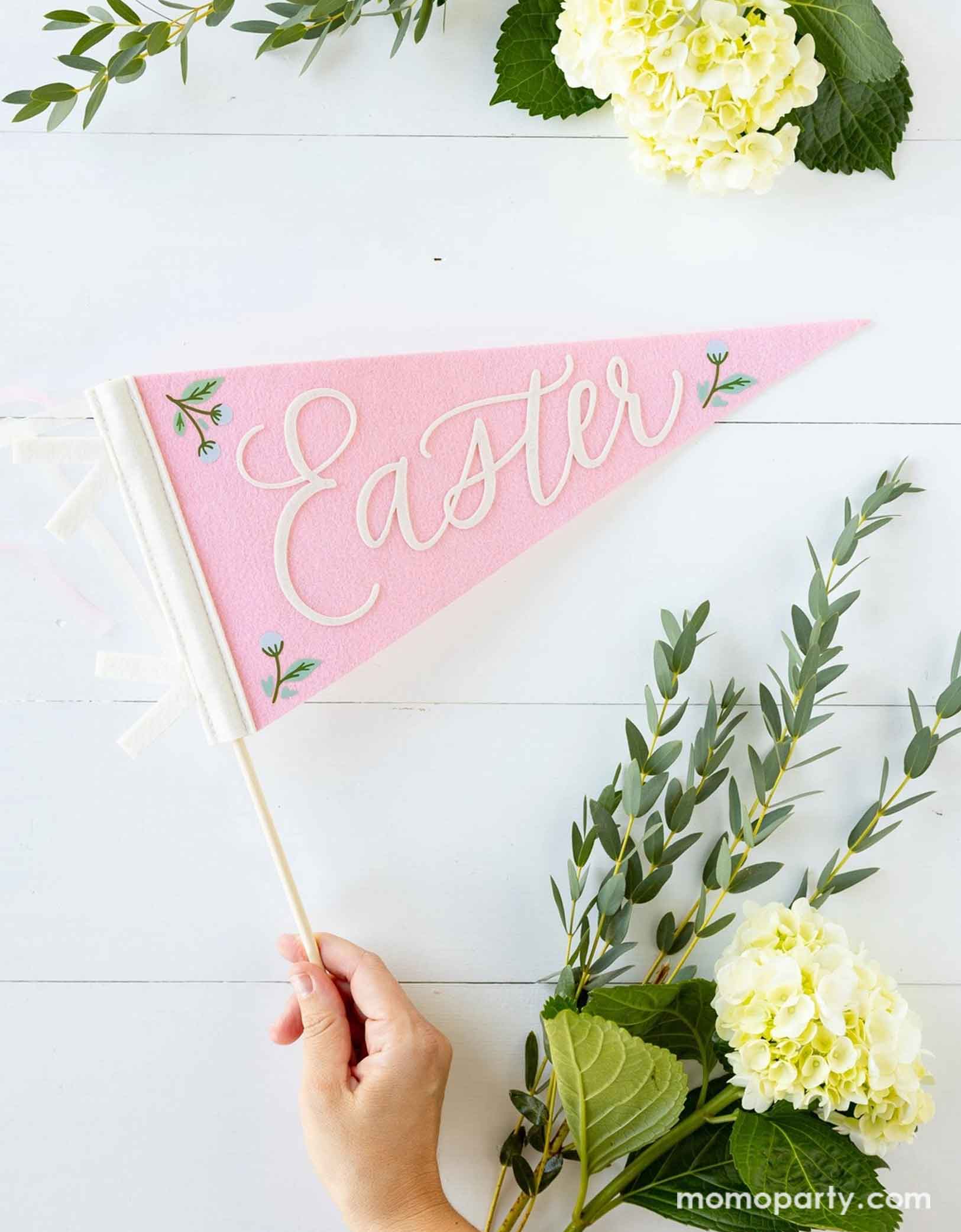 A lady's hand holding Momopartys's 15" pink felt pennant banner features the words "Easter" in fun, playful letters. Around the pennant there are some spring floral bouquet, a perfect inspiration for spring or Easter celebration!