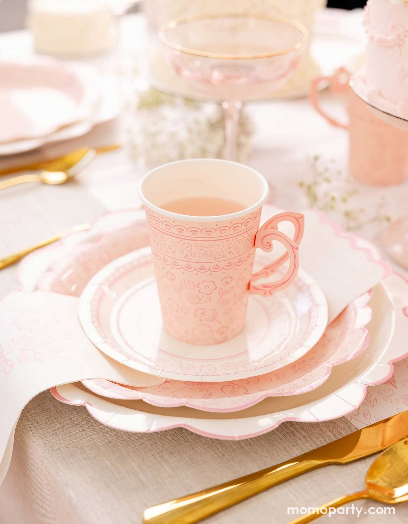 An elegant placeset featuring Momopartys's Pink Pembroke tableware collection including the 12" Pembroke Pink Edge Scallop Plates paired, 9" Pembroke Pink floral Plates, 7" Pembroke Pink Plates, Pembroke Pink napkins and the 12oz party cups. Underneath the plates is the Pembroke Pink floral paper table runner. With the gold foil utensil set, a pretty floral arrangement and pastel pink butter cakes and glasses of rose champagne, this table setting is perfect for a spring Easter inspired celebration.