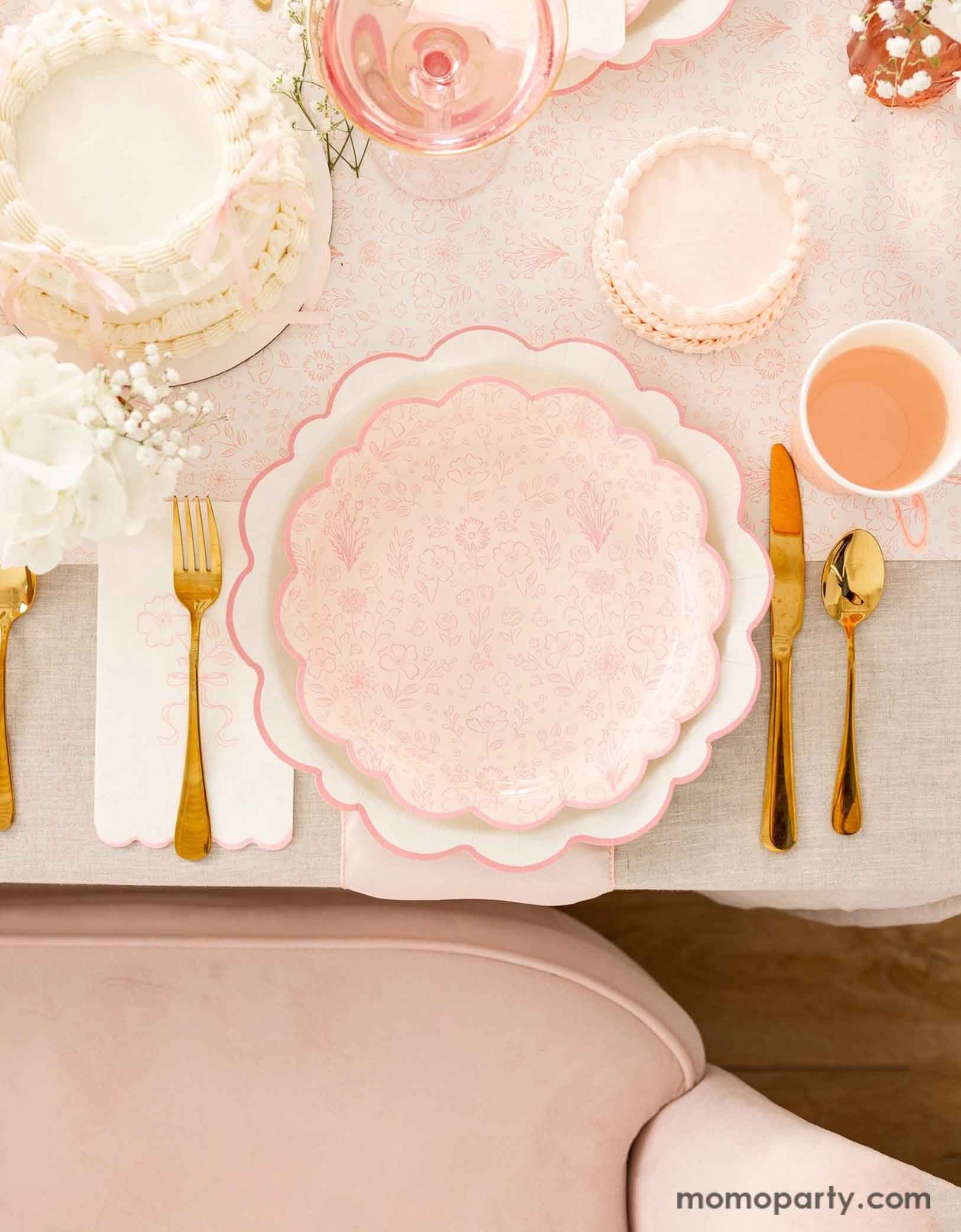 A beautiful and elegant tablescape featuring Momopartys's Pink Pembroke tableware collection including the 12" Pembroke Pink Edge Scallop Plate paired with 9" Pembroke Pink floral Plate and Pembroke Pink Edge Scallop Napkin. Underneath the plates is the Pembroke Pink floral paper table runner. With the gold foil utensil set, a pretty floral arrangement and pastel pink butter cakes and a glass of rose champagne, this table setting is perfect for a spring inspired celebration, be it Easter or Mother's Day.