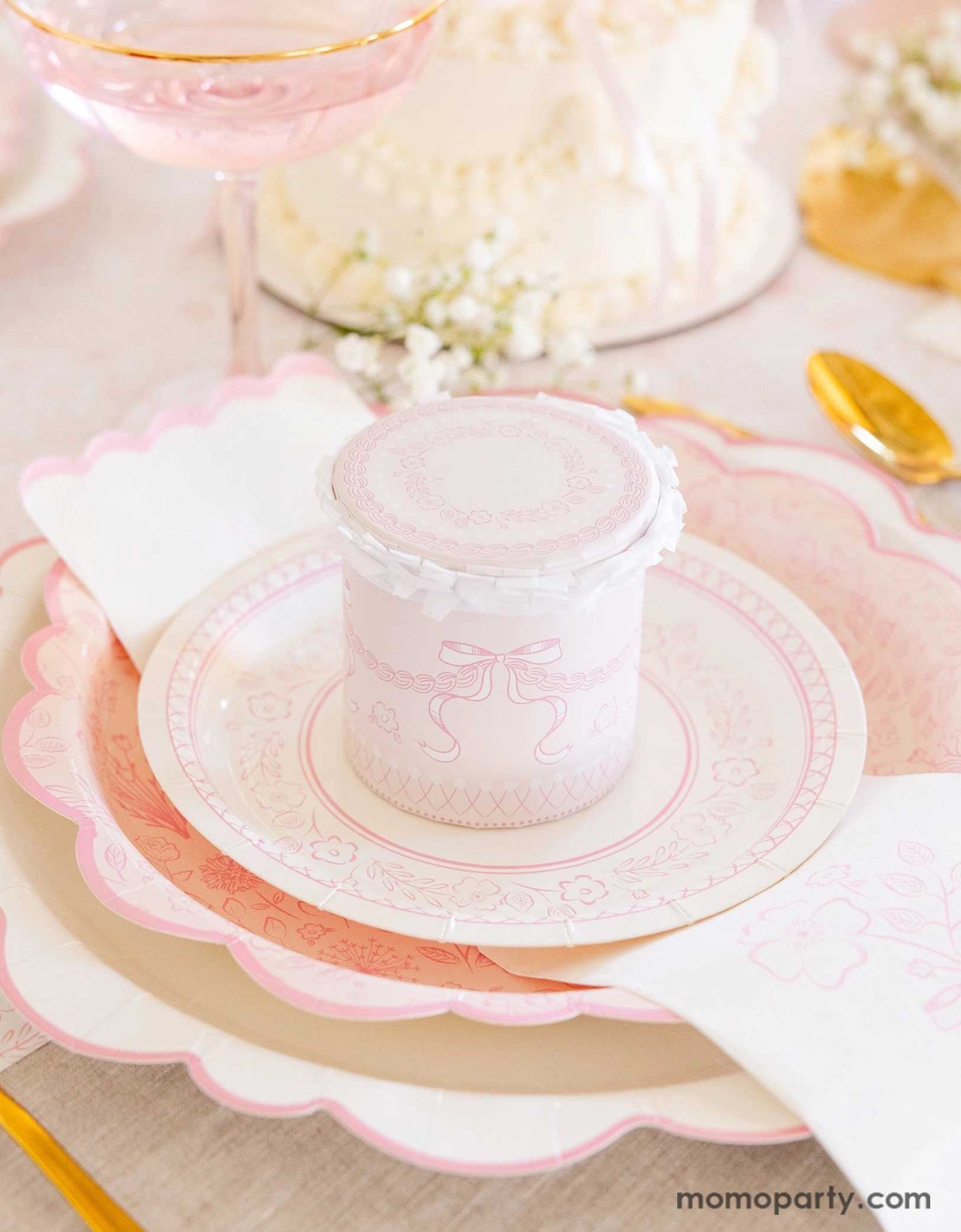 An elegant placeset featuring Momopartys's Pink Pembroke tableware collection including the 12" Pembroke Pink Edge Scallop Plate paired, 9" Pembroke Pink floral Plate, 7" Pembroke Pink Plate, and the Pembroke Pink napkin. With the gold foil utensil set, a pretty floral arrangement, a pink buttercream cake and a pink champagne glass, this table setting is perfect for a spring inspired celebration, be it an Easter celebration or Mother's Day party.