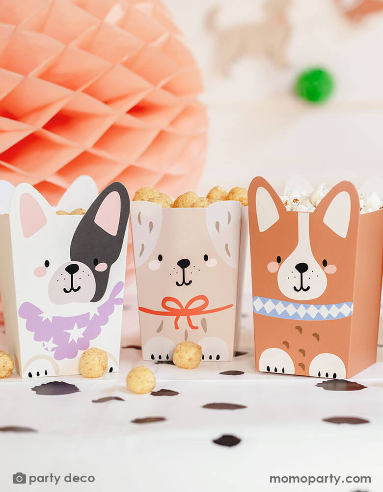 An adorable dog puppy themed birthday party table featuring Momopartys's Puppy Dog Party Snack Treat Boxes by Party Deco. These snack boxes come in 4 designs of different puppies with adorable dog design on it. They're filled with popcorn, chips and treats placed on the Dalmatian printed dot tablecloth underneath, with pastel honeycomb decorations around the table and a happy birthday banner in the back, this makes a cute scene for kid's dog themed birthday party celebration.