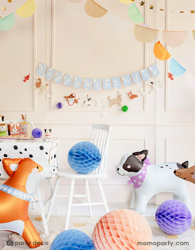 An adorable dog themed birthday part decoration set up featuring Momopartys's dog themed party goods including dog happy birthday party banners, honeycomb decorations, dog shaped standing foil balloons, dog shaped party cups, party snack boxes on an adorable Dalmatian dotted tablecloth. The soft colors brings a cute touch to this party set up making it perfect for younger kids who love dogs. 