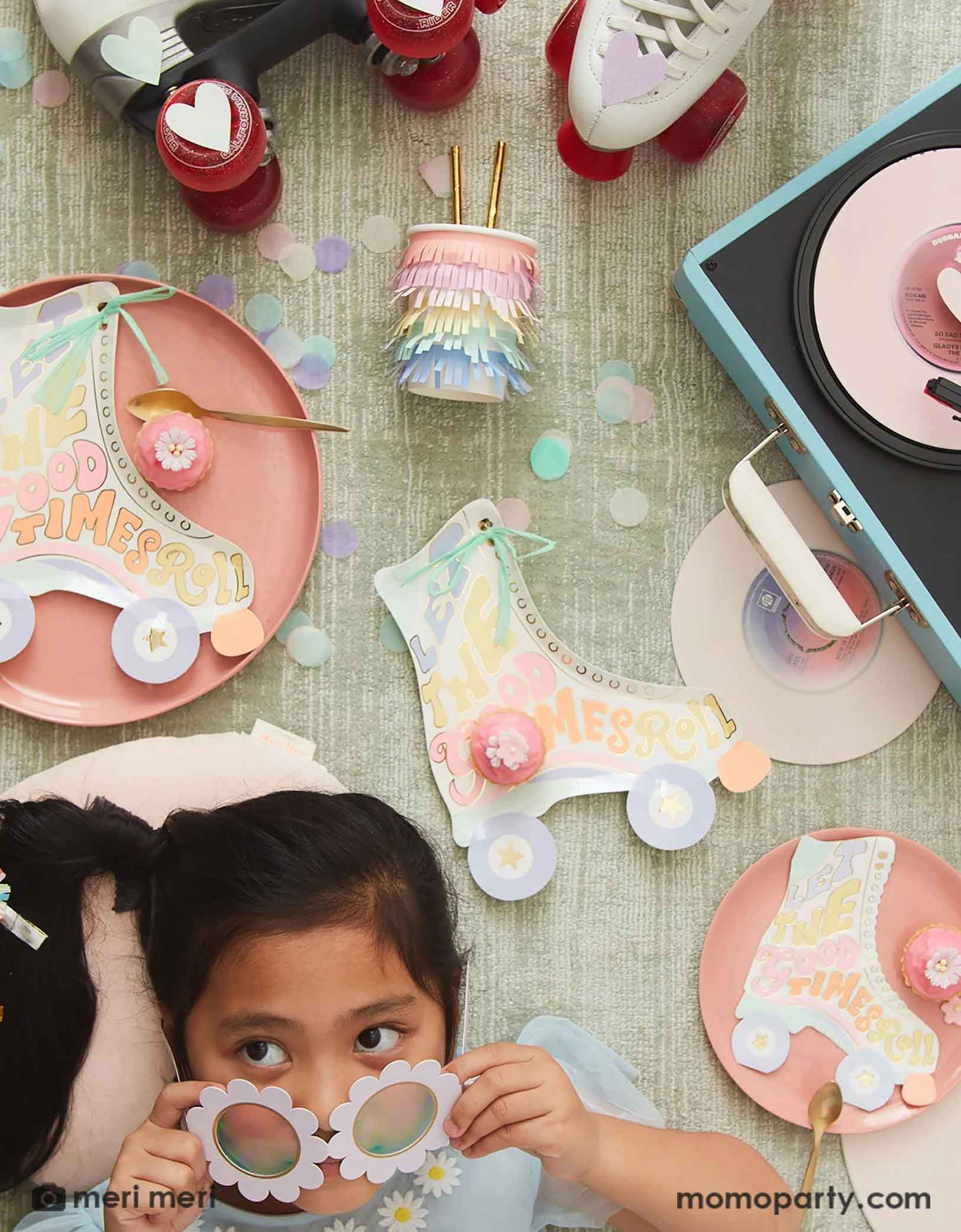 A little girl wearing a white daisy shaped sunglasses lying on the ground with some retro roller skates and a vintage record player with Momopartys's Roller Skate shaped Party tablewares including napkins, plates and party cups around. With pastel confetti spread across, this makes a festive scene for a retro inspired celebration for kids!