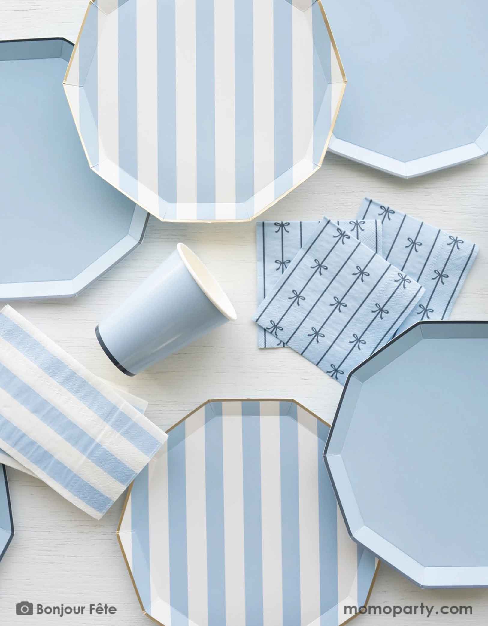 An overhead shot of a party table filled with Momopartys's pastel blue themed party tableware including sky blue cabana striped dinner plates, napkins and pastel blue dinner plates in decagon shape with matching napkins with bows and party cups - a great collection for boy's birthday or a baby boy shower.