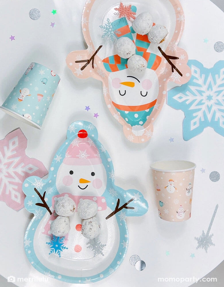 A winter snow day themed party table featuring two snowman shaped plates and coordinating party cups and snowflake shaped napkins, on the plates, there are some donut hole desserts topped with Momopartys's snowflake acrylic picks in four beautiful colors of sliver, blue, teal and pink, with the pastel pallet, this makes a darling winter themed tablescape for kid's birthday party.