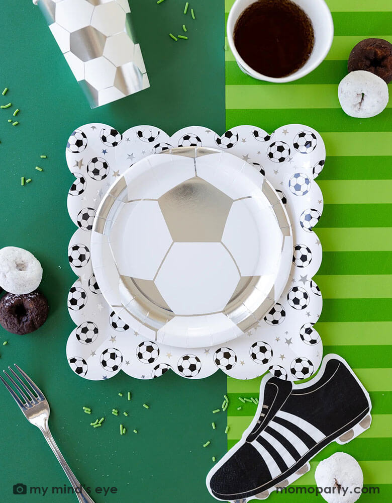 A fun soccer themed party table featuring Momopartys's soccer party collection including silver soccer shaped plates and party cups, cleat shaped napkins and soccer table runner by My Mind's Eye. With some snacks, green sprinkles around, this makes a great inspo for a fun kid's soccer themed birthday party or a championship celebration!