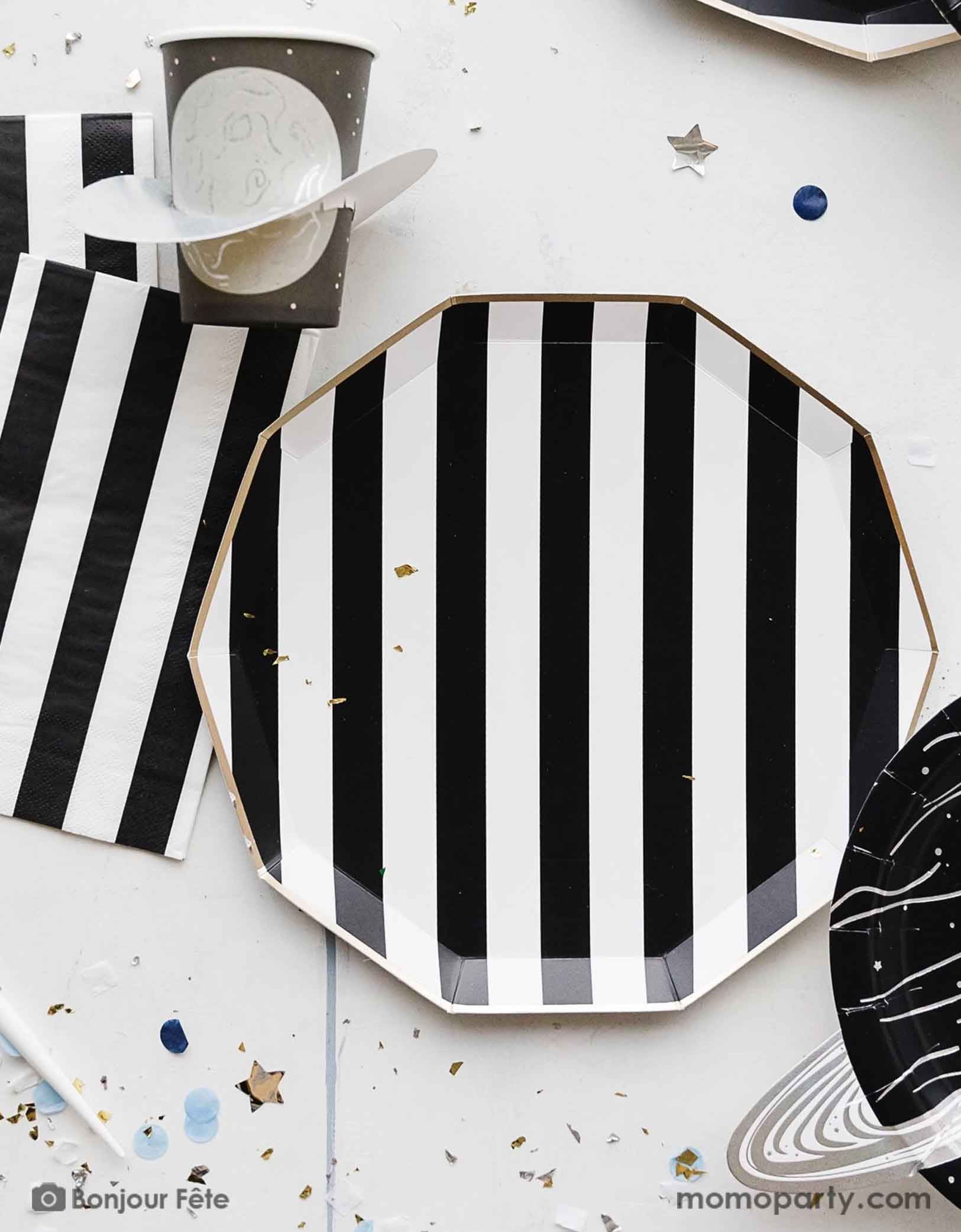 A space themed party table featuring Momopartys's Black Striped Party Supplies including paper dinner plates, guest towels, black and white cutlery set. With the planet 3D party cup and metallic star confetti around the table, this makes a perfect inspo for a chic, stylish and modern space themed celebration.