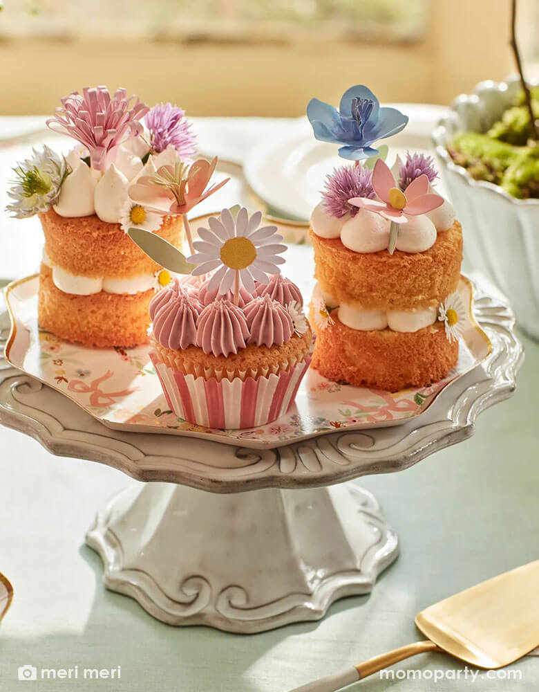 An elegant spring inspired party table featuring a vintage ceramic cupcake stand which hold some beautiful cupcakes and desserts topped with Momopartys's flower garden cupcake toppers by Meri Meri. With Momopartys's elegant floral side plate below it, it makes a darling inspiration for a spring gathering or Easter celebration.