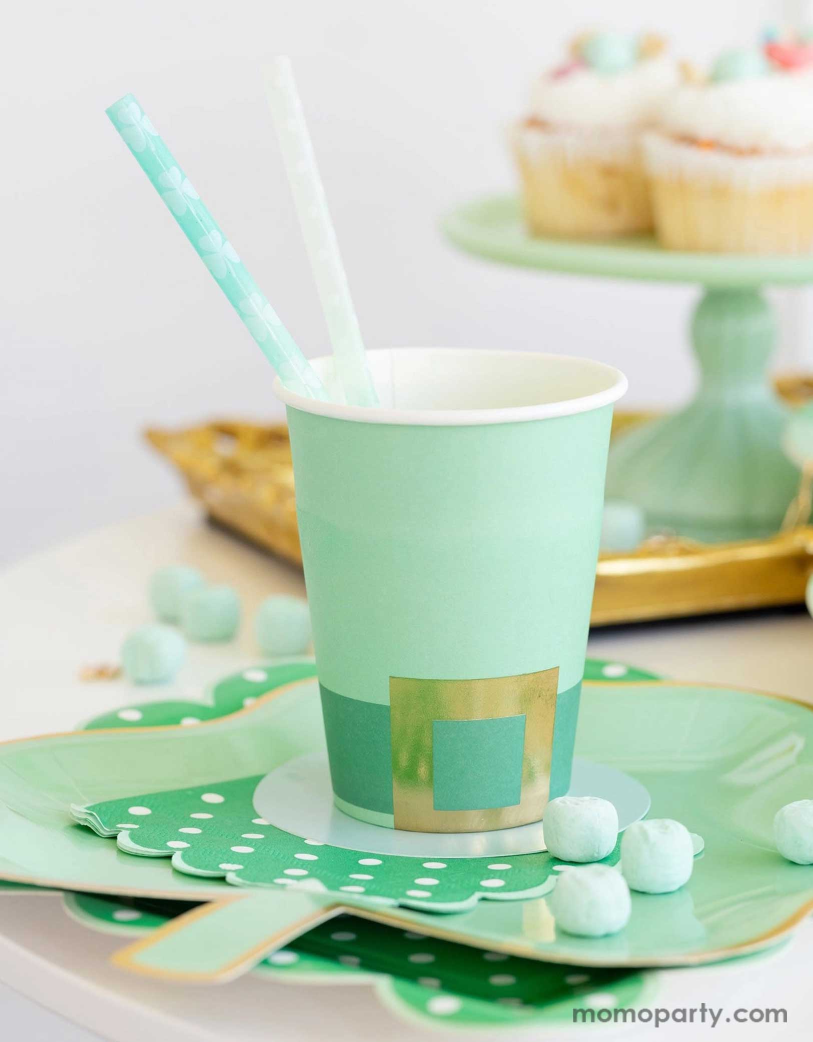A cheerful St. Patrick's Day party table featuring Momopartys's St. Patrick's Day themed party supplies including the Leprechaun hat party cup, green polka dot napkins, shamrock shaped paper plates, and shamrock reusable straws. In the back there's a green cake stand with cupcakes on a gold serving tray - a great inspo for a fun and festive St. Patrick's Day celebration.