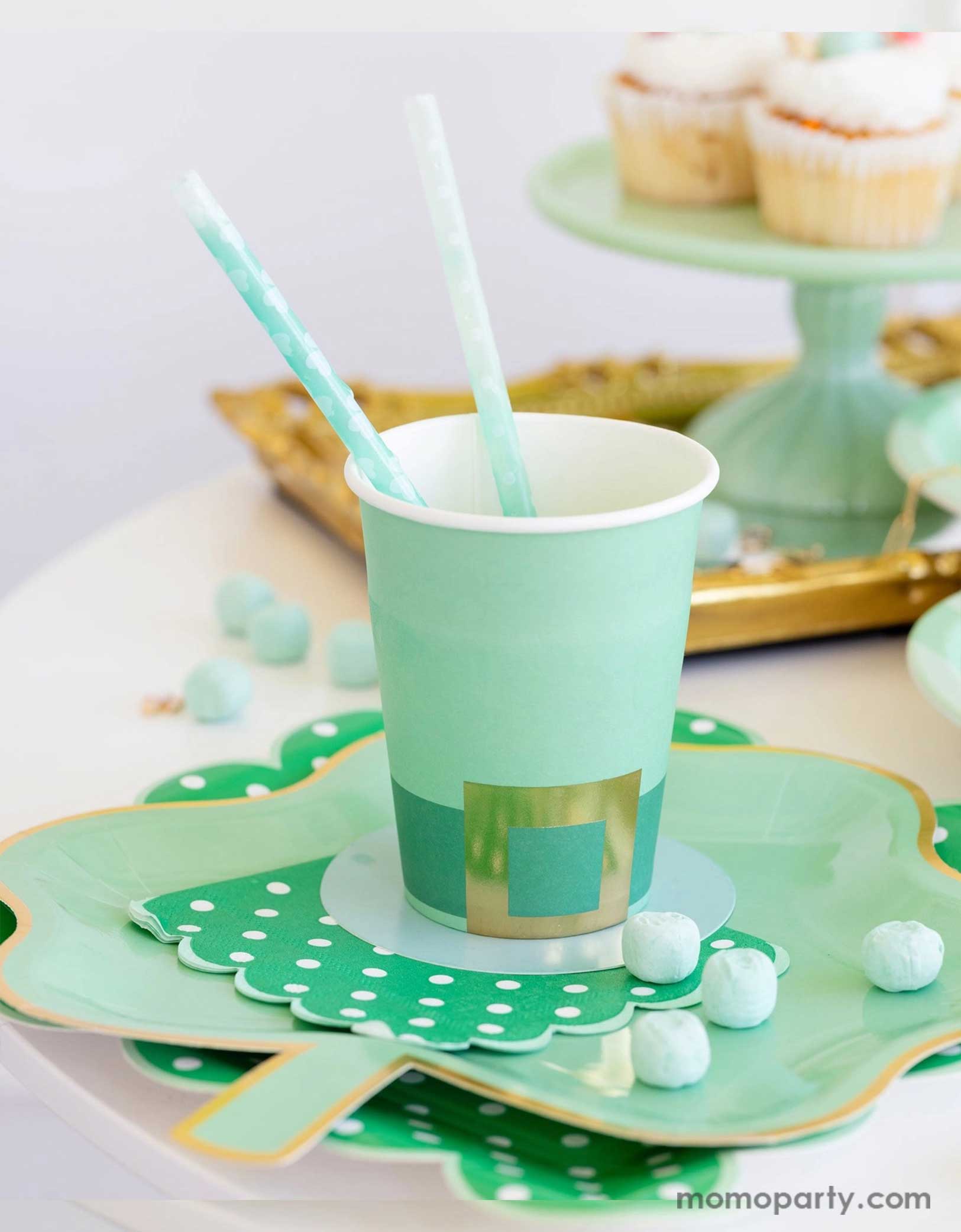 A cheerful St. Patrick's Day party table featuring Momopartys's St. Patrick's Day themed party supplies including the Leprechaun hat party cup, green polka dot napkins, shamrock shaped paper plates, and shamrock reusable straws. In the back there's a green cake stand with cupcakes on a gold serving tray. With green candies around this table makes a great inspo for a fun and festive St. Patrick's Day celebration.