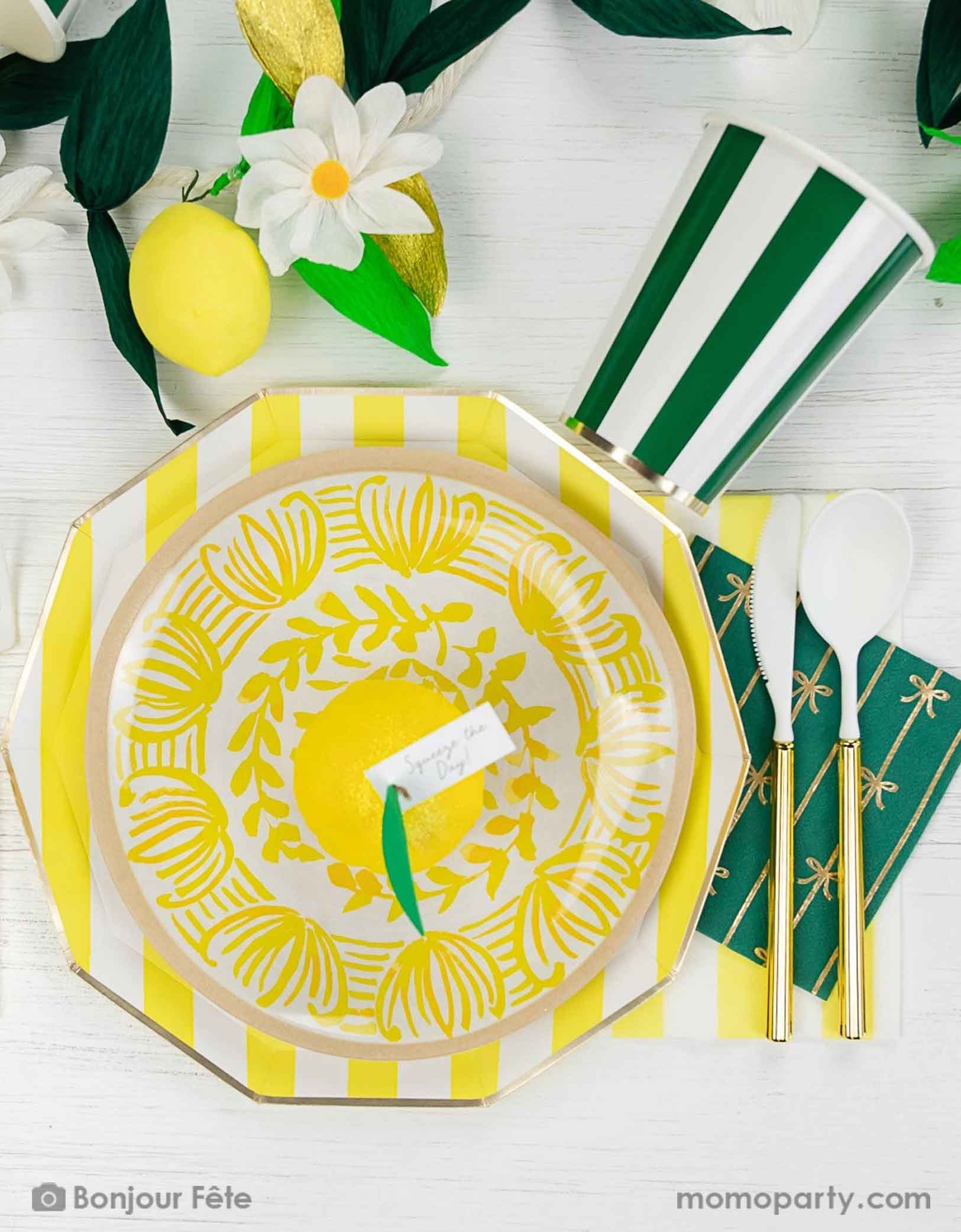 An elegant summer Capri lemon themed party tablescape featuring Momopartys's cabana striped party tableware in yellow and green including table plates, cups and napkins. On the table there's a summer party garland with flowers, greenery, lemons as decorations. 