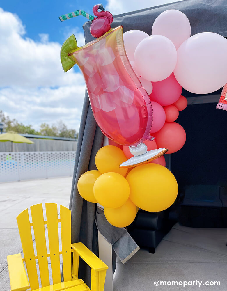 Summer Pool Party by Momopartys. Enjoy a poolside tent adorned with the 'Let's Flamingo Drink Foil Mylar Balloon' and coral, pink, goldenrod, and rose latex balloons. A bright yellow outdoor chair completes the vibrant summer vibe. Perfect for your summer bash!