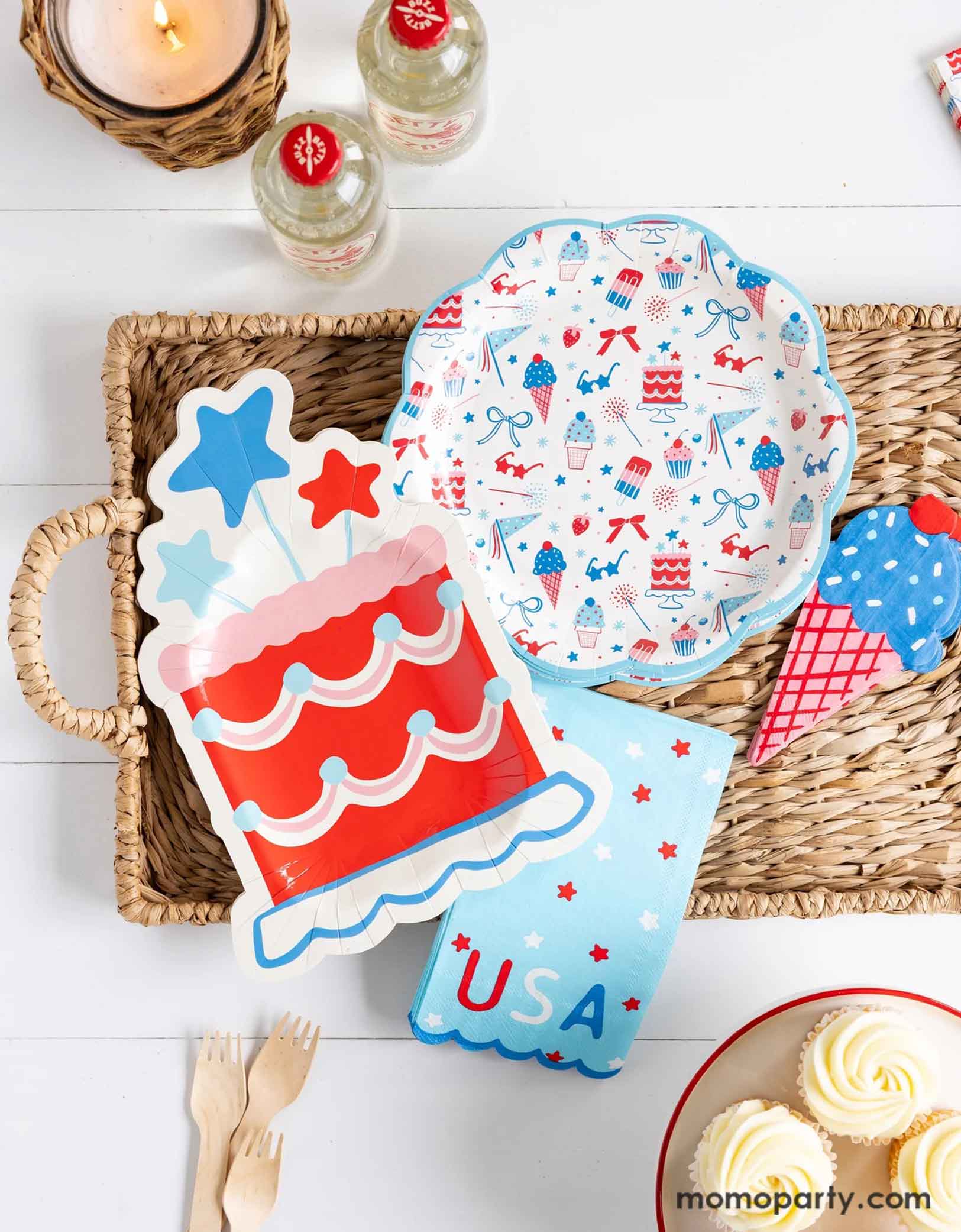 An overhead shot of a patriotic themed celebration featuring Momopartys's Summertime pattern plates, napkins, cake shaped paper plates, and ice cream shaped dinner napkins on bamboo woven tray. Around the tray there are some white buttercream cupcakes, some wooden forks and a couple of soda bottles in red, making this a great party inspo for a Fourth of July party, a Memorial Day BBQ or any patriotic summer celebrations!