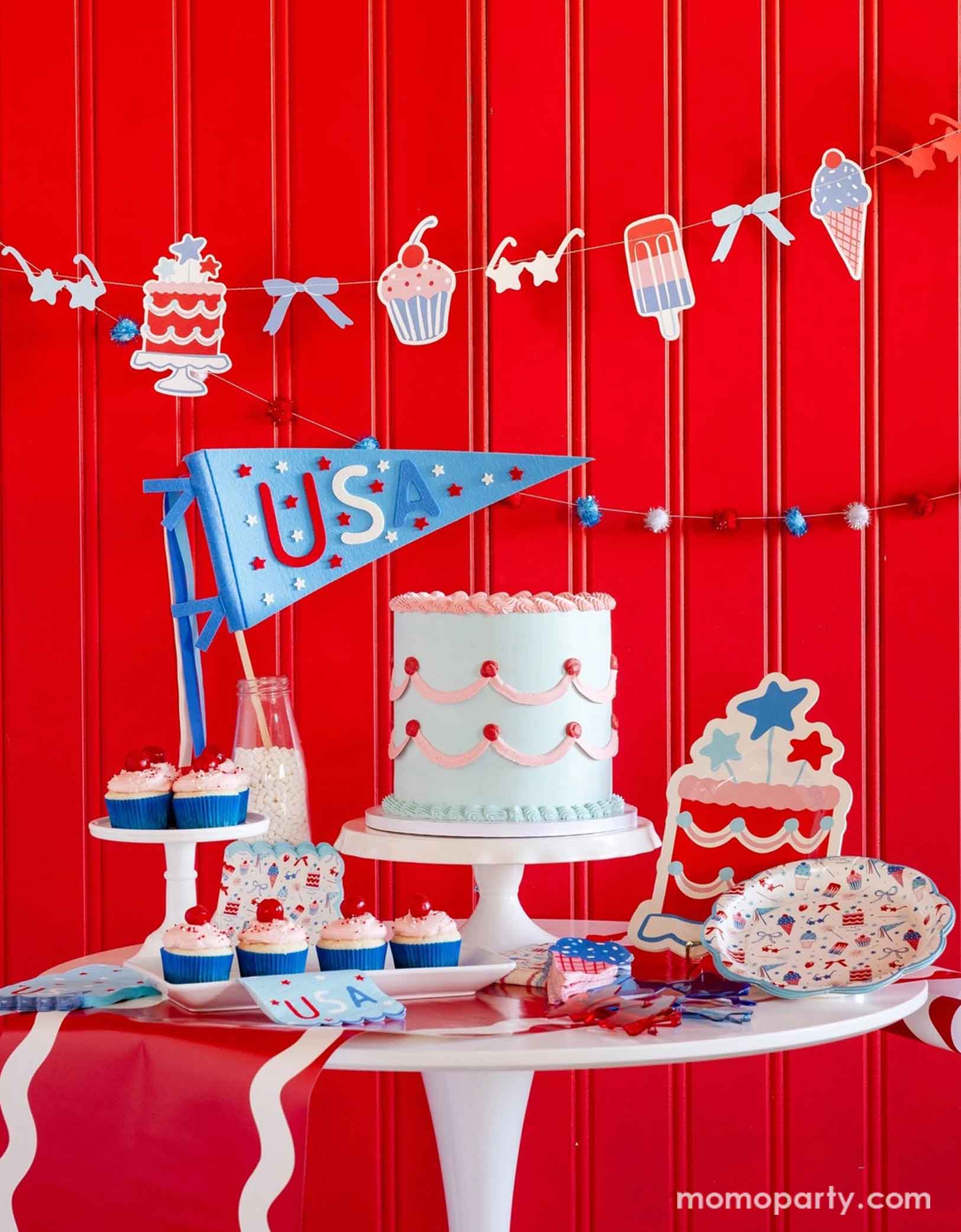 A festive patriotic party set up featuring various Fourth of July themed party decors from Momopartys including party banner with summer themed party pennants including popsicles, ice cream, cupcake, cakes, and star shaped sunglasses in red, blue and white colors. On the table there's a vintage pastel blue buttercream cake along with some cupcakes with cherries on top, along with a USA felt pennant and patriotic party tableware including party plates, napkins and a table runner, for a fun summer party.