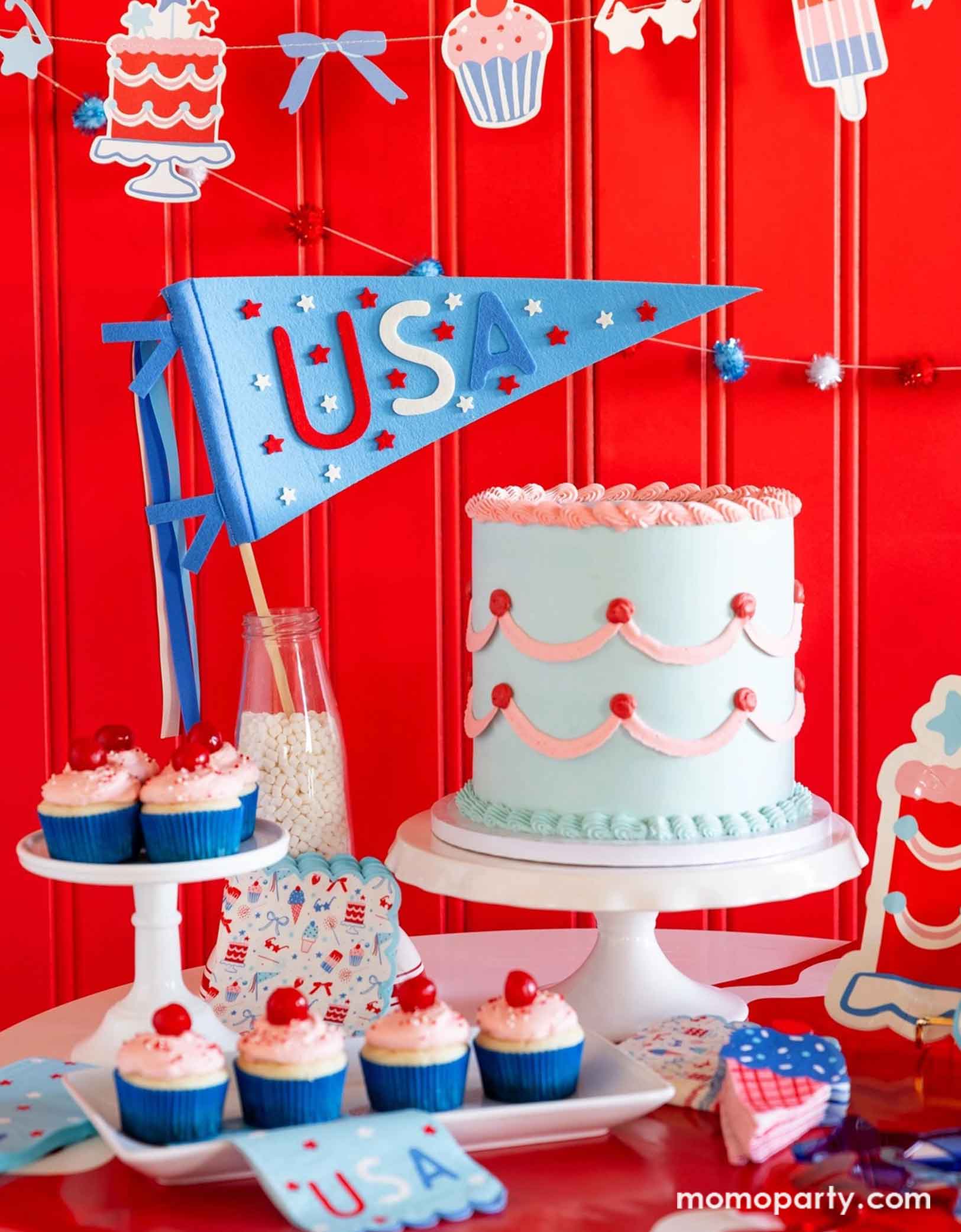 A festive patriotic party set up featuring various Fourth of July themed party decors from Momopartys including party banner with summer themed party pennants including popsicles, ice cream, cupcake, cakes, and star shaped sunglasses in red, blue and white colors. On the table there's a vintage pastel blue buttercream cake along with some cupcakes with cherries on top, along with a USA felt pennant and patriotic party tableware including party plates, napkins and a table runner, for a fun summer party.