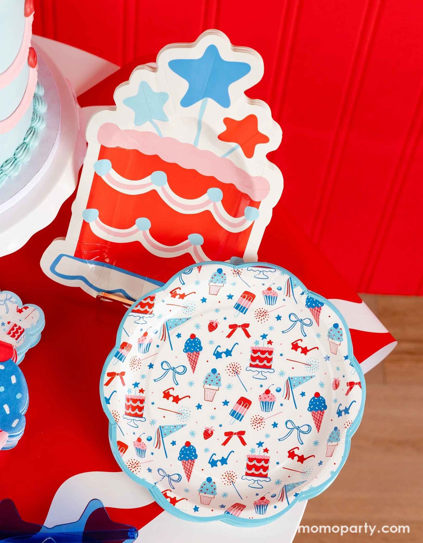 An overhead shot of a patriotic themed celebration featuring Momopartys's Summertime pattern plates, napkins, cake shaped paper plates, and ice cream shaped dinner napkins on a red paper table runner. The pattern features summer element icons in red, white and blue, perfect for a Fourth of July party, a Memorial Day BBQ or any patriotic summer celebrations!