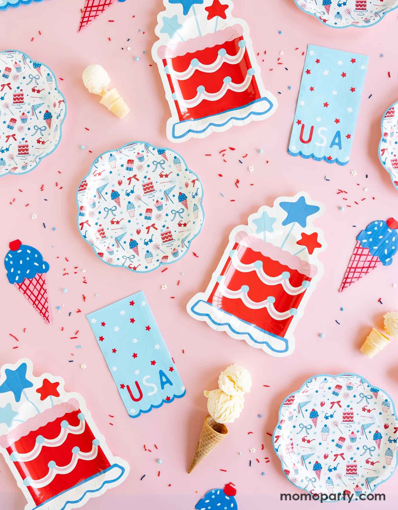 An overhead shot of Momopartys's Summertime tableware collection including pattern plates, napkins, cake shaped paper plates, ice cream shaped dinner napkins and USA blue guest towel napkins on a pink table. Around the tableware there's red, white and blue sprinkles and some ice cream cones. These tableware are perfect for a Fourth of July party, a Memorial Day BBQ or any patriotic summer celebrations!