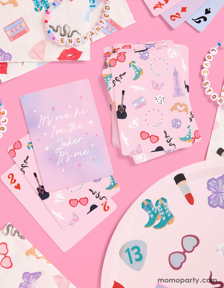 A tablescape of Momopartys's Taylor Swift Era Tour party collection featuring Momopartys's Taylor Swift playing cards, 9" x9" party plates, 5" napkins featuring Taylor Swift inspired designs including red lipstick, red lips, butterflies, cowgirl boots, snakes, cassette tapes, guitar picks, heart hand symbols, and heart shaped sunglasses. With a couple of friendship bracelets, this is a perfect inspiration for a fun Swiftie's birthday party!