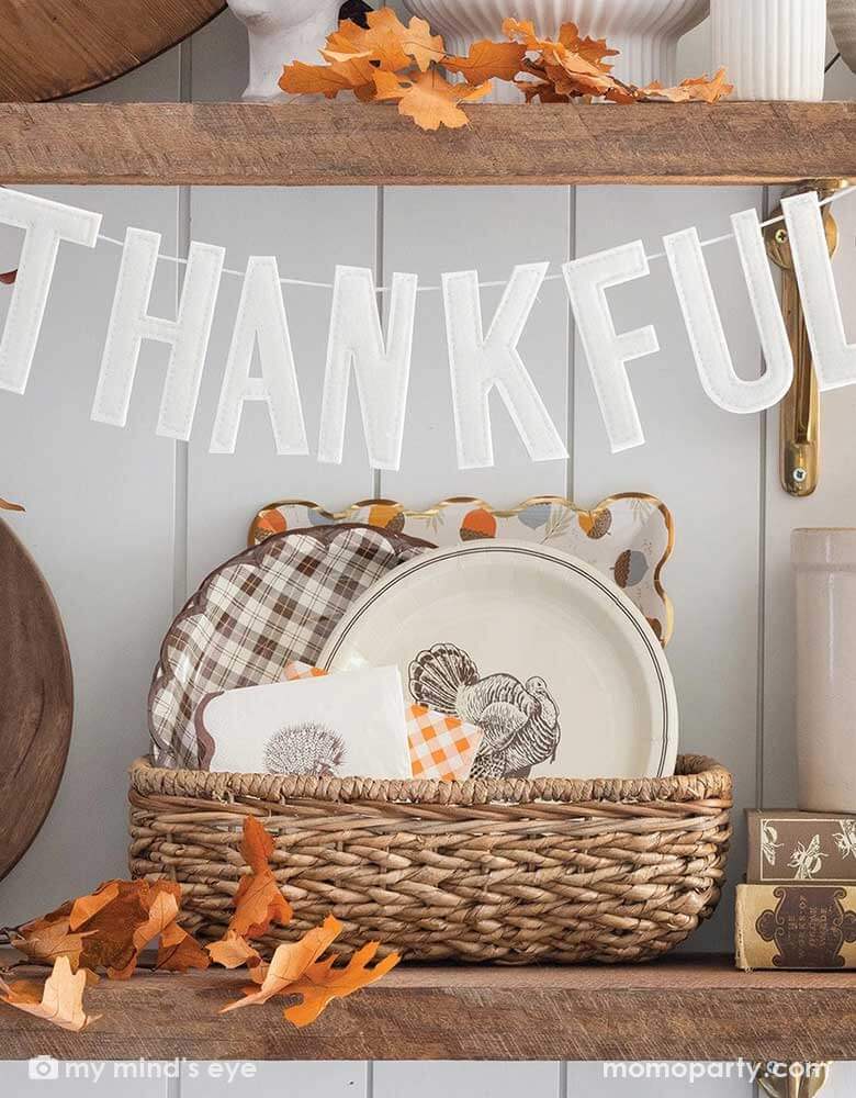 A kitchen shelf filled with fall themed tableware and decorations, on the self Momopartys's 3' "Thankful" puffy felt banner by My Mind'e Eye, which is hung across, makes it a perfect inspiration for fall home decor.