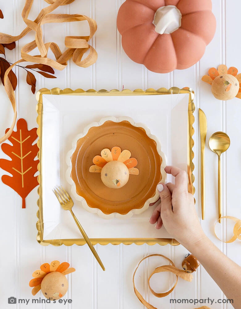 A beautiful and playful Thanksgiving tablescape features Momopartys's Thanksgiving party supplies including fall inspired paper plates, oak leaf shaped napkins and turkey surprise balls. A perfect inspo for a modern Thanksgiving dinner tableset in this harvest season.