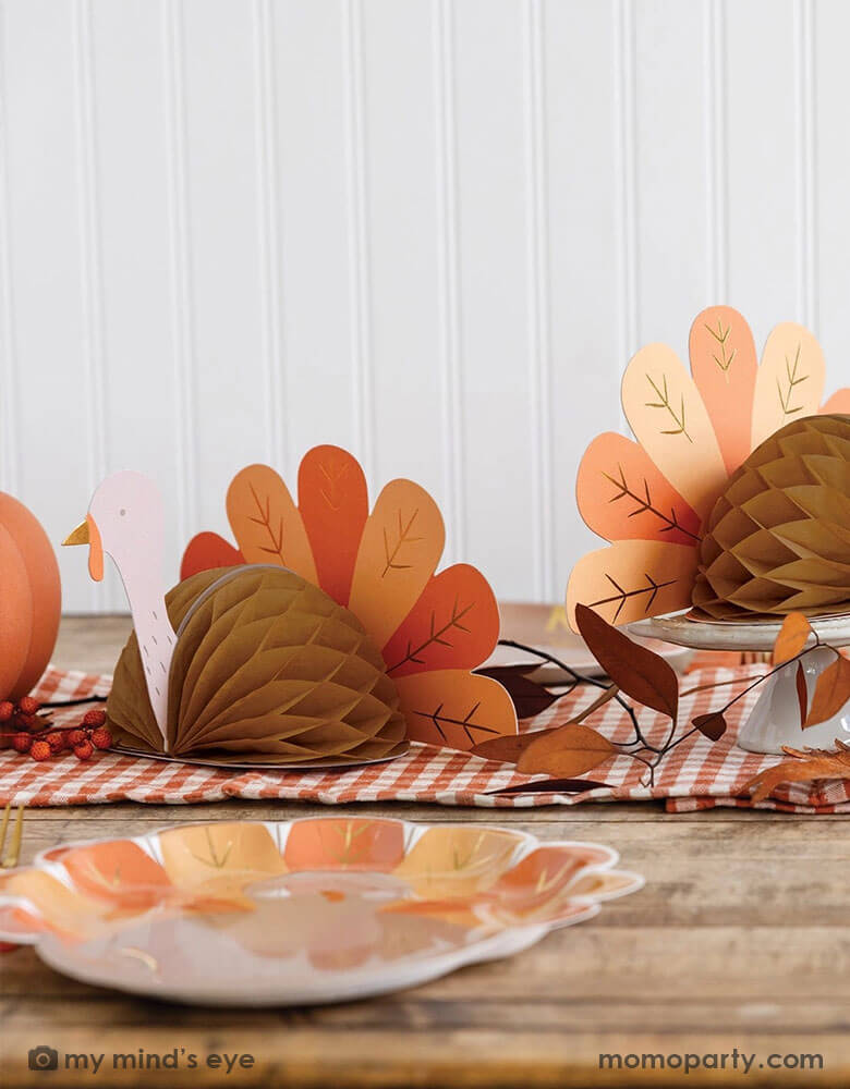 A fall inspired party table features Thanksgiving party supplies by Momopartys including the turkey shaped plates, oak leaf shaped napkins and turkey honeycomb decorations as the centerpiece. With some fall leaf and acorn decorations spread across, this makes a perfect inspo for an autumn gathering or Thanksgiving dinner decor this harvest season.