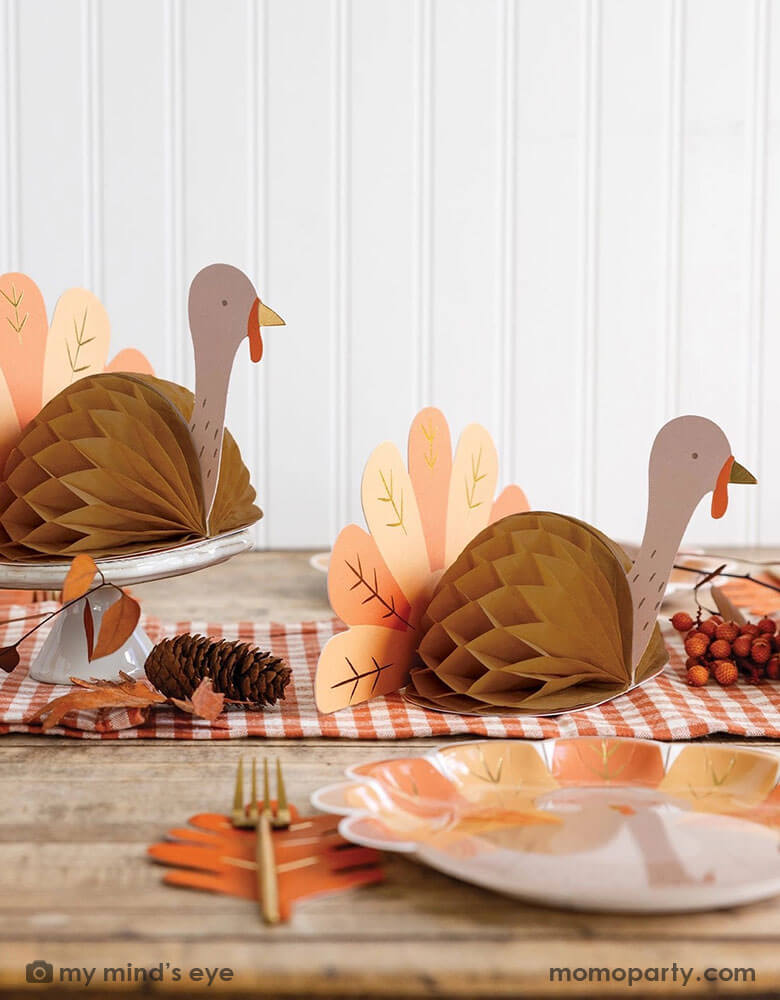A fall inspired party table features Thanksgiving party supplies by Momopartys including the turkey shaped plates, oak leaf shaped napkins and turkey honeycomb decorations as the centerpiece. With some fall leaf and acorn decorations spread across, this makes a perfect inspo for an autumn gathering or Thanksgiving dinner decor this harvest season.