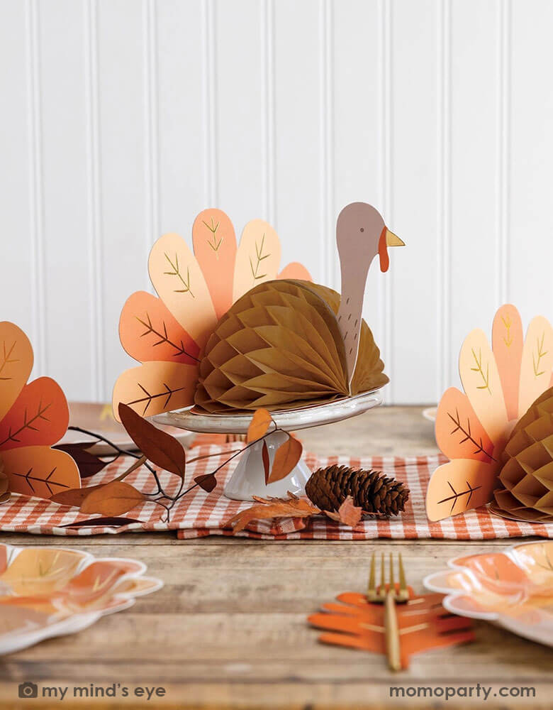 A fall inspired party table features Thanksgiving party supplies by Momopartys including the turkey shaped plates, oak leaf shaped napkins and turkey honeycomb decorations as the centerpiece. With some fall leaf and acorn decorations spread across, this makes a perfect inspo for an autumn gathering or Thanksgiving dinner decor this harvest season.