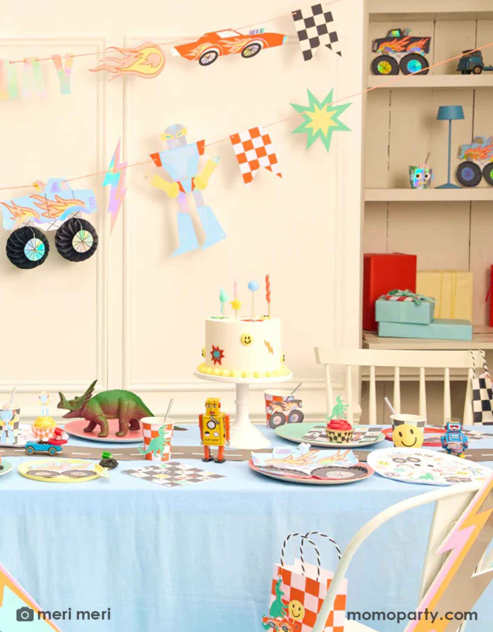 A fun themed kid's birthday party decorating set up featuring Momopartyss Momopartys's Toybox Party Collection by Meri Meri. With the retro inspired and checker board designs,  featuring elements from kid's toy boxes including dinosaurs, monster trucks, race cars, googly eyes. robots and lightning bolts, these party supplies including a large party garland on the way with HAPPY BIRTHDAY message, and a table of fun and festive party tableware including party plates, cups, napkins and favor bags.