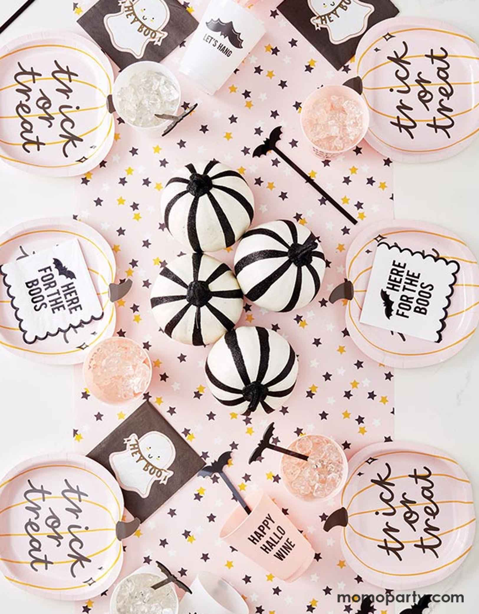 A festive pink Halloween party table featuring adorable girly Halloween themed party supplies form Momopartys including the trick or treat pumpkin shaped plates, pastel pink star table runner, Hey Boo ghost napkins and Here for the Boos bat napkins, making this a playful and fun table setting for a not-so-spooky Halloween celebration.